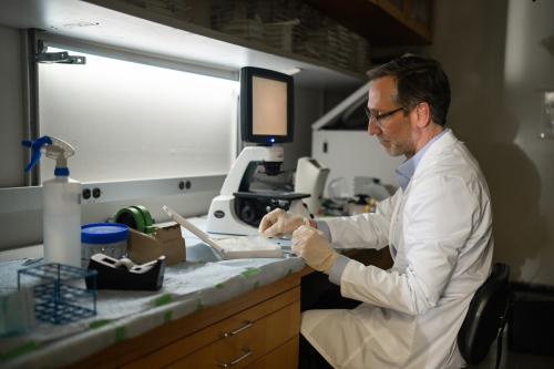 Dr. Antoni Ribas examines a biopsy slide in his UCLA lab, wearing gloves and a white lab coat.