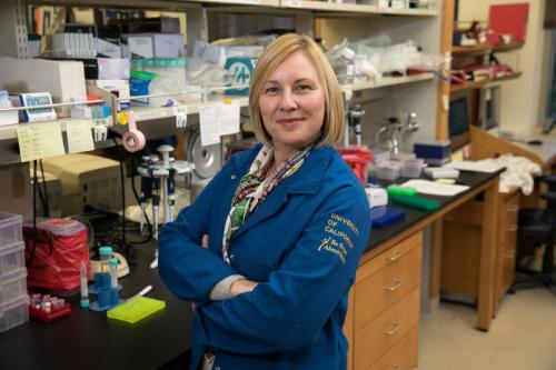 Researcher Amander Clark stands in her lab with her arms crossed and smiles for a photograph.