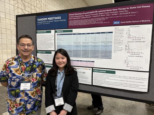 A photograph of Drs. Kohn and Prueksapraopong standing before a poster sharing the abstract for the clinical trial detailed in this press release. Dr. Kohn wears a colorful tropical shirt and Dr. Prueksapraopong wears a blue shirt with a black blazer. 
