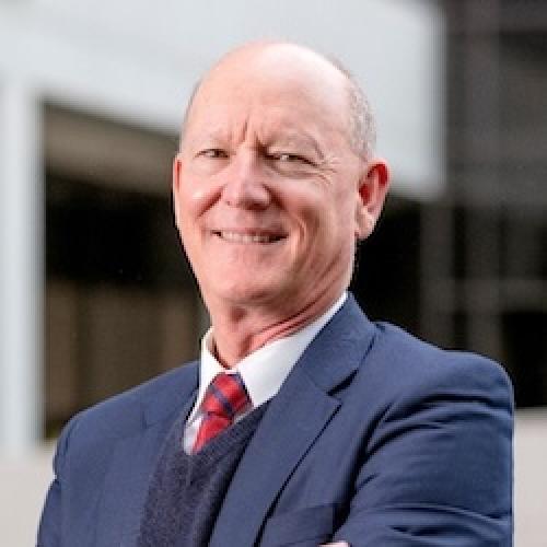 Professional headshot of Paul W. Noble, M.D., wearing a blue suit with red patterned tie, smiling against a blurred background