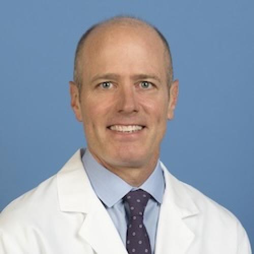 Professional headshot of S. Thomas Carmichael, M.D., Ph.D., wearing a white medical coat and blue patterned tie against a blue background