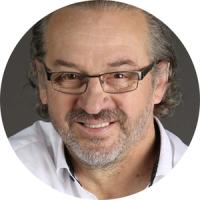 Professional headshot of a man with glasses and gray beard wearing a white shirt, smiling