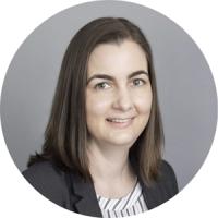 Professional headshot of a woman with shoulder-length brown hair wearing a dark blazer over a striped blouse