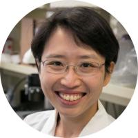 Headshot of Yvonne Chen, a woman with short dark hair wearing glasses and a white lab coat, smiling in a laboratory setting.