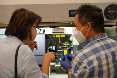 Two individuals photographed from behind, conversing in a UCLA lab. 