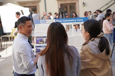 Event participants gather around a poster board in a UCLA courtyard.