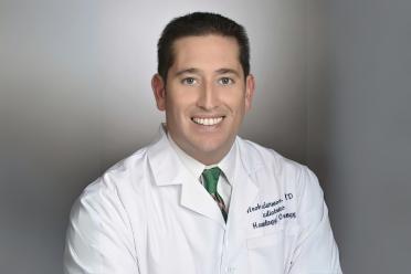 A doctor in a whitecoat smiles for a headshot.