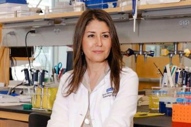 Dr. Sanaz Memarzadeh in white lab coat standing in research laboratory with equipment and supplies visible in background.