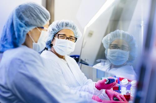 Two researchers in full PPE at work in a UCLA lab. One smiles at the camera.