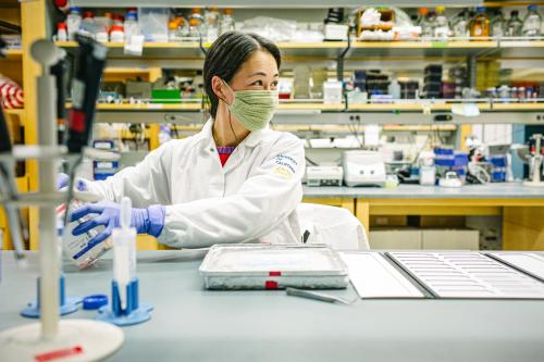 A UCLA researcher with smiling eyes looks out of frame while working in a laboratory. 