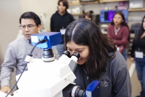 female high school student wearing a grey disneyland hoodie looks through a microscope