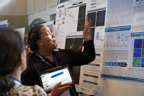 a scientist holding an ipad points at a research poster
