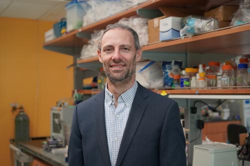 UCLA scientist Peter Clark smiles in his lab wearing a checkered shirt and dark grey suit jacket.