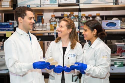 Brigitte Gomperts smiles and hold samples in a UCLA lab beside two members of her lab.