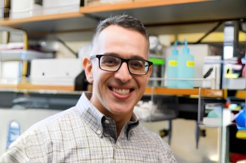 Headshot of Dr. Albert Almada in glasses and a plaid button up shirt in his lab