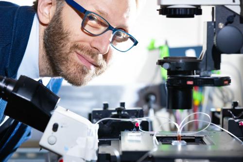 UCLA Scientist Dino Di Carlo leans over equipment in a lab and smiles at camera. 