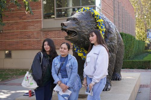 three female high school students pose for a photo in front of the bruin bear statue on the ucla campus
