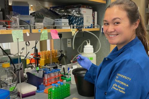 Woman in blue lab coat smiling while working with laboratory equipment and test tubes