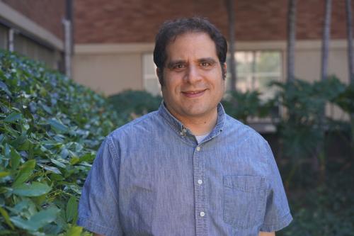 UCLA scientist Jason Ernst smiles for a photograph. He wears a blue collared short-sleeve shirt and stands outdoors on the UCLA campus.