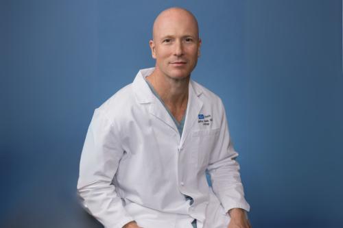 Jeffrey Veale smiles for a photograph. He dons a white labcoat.