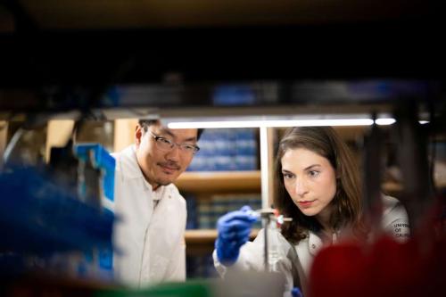 A photo that shows Dr. John Lee and Galina Semenova in a laboratory, working together on setting up lab equipment. Both scientists are dressed in white lab coats. 