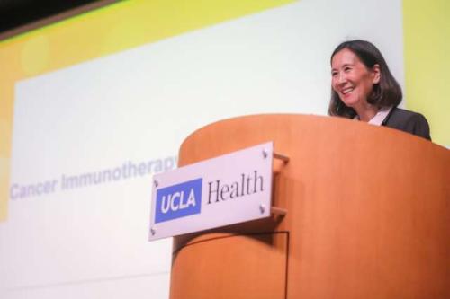Dr. Linda Liau smiling behind a podium with a UCLA Health plaque on it.