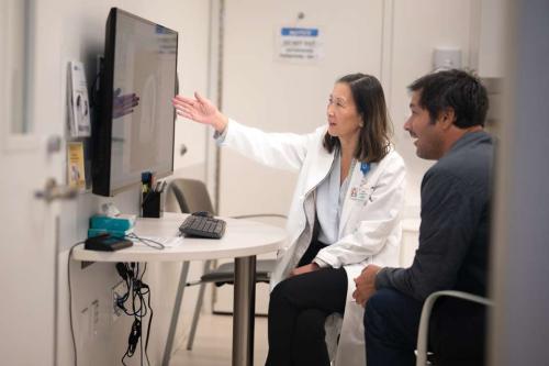 Dr. Linda Liau points to a screen while sitting with a patient