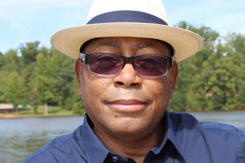 Close-up of Melvin Mann in dark blue shirt, sunglasses and straw fedora