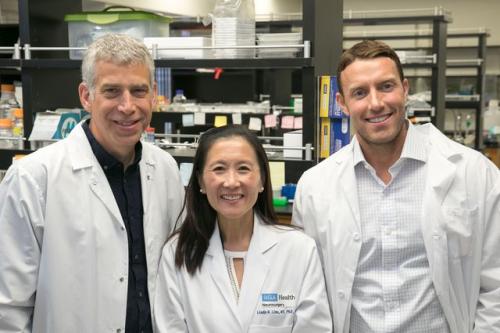 Thomas Graeber, Dr. Linda Liau, and David Nathanson standing together in white lab coats in a laboratory setting, smiling at the camera.