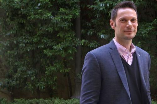 Patrick Allard stands smiling before deep green trees.