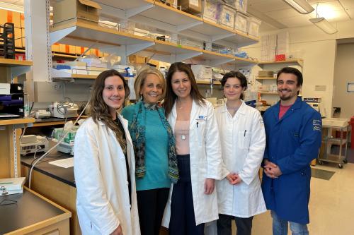 A group of researchers stand smiling in a lab with a donor and patient advocate. 