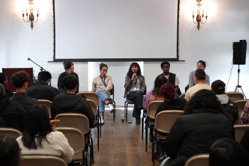 five panelists sitting down in front of a room in front of seated high school students