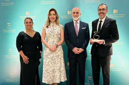 Four people pose at King Hussein Cancer Research Award ceremony; the person on the right holds an award trophy.