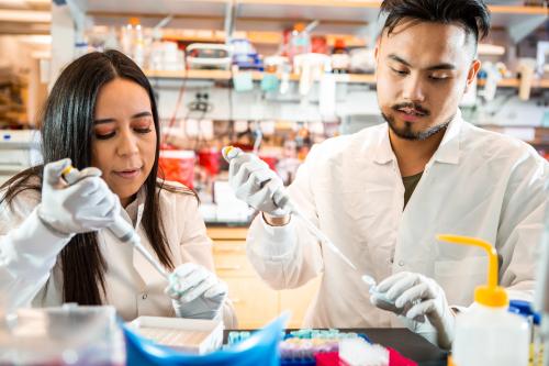 A male and female researcher stand side by side pipetting in a UCLA lab 