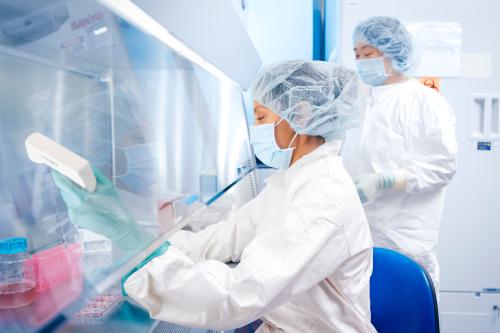 Two female scientists work at a hood in a GMP facility in UCLA.