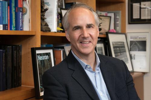 Daniel Geschwind smiles for a photo in his office, books lining the walls behind him.