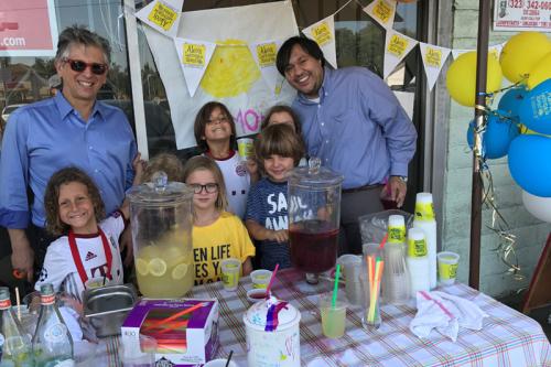 Children take a photo in front of lemonade stand with UCLA researcher.