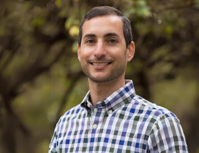 A man smiles at the camera while standing outdoors.