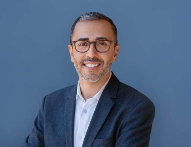 UCLA's Dr. Mina Sedrak smiles for a headshot wearing glasses and a light blue shirt with dark blue blazer.