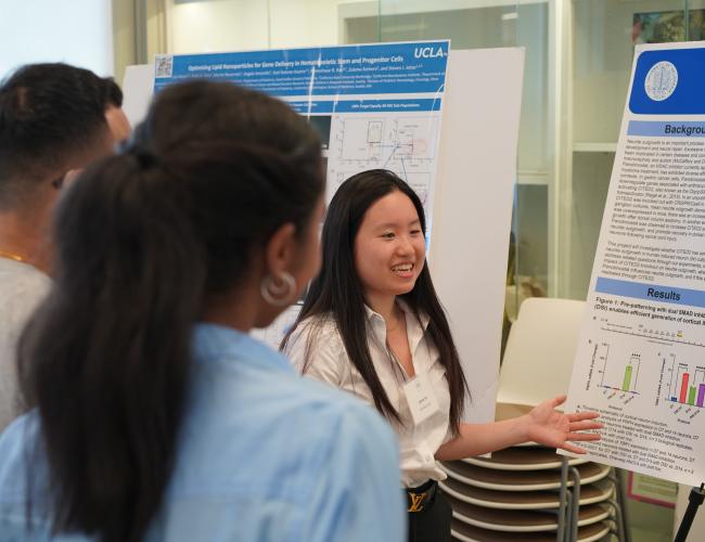 Students participate in the UCLA BSCRC's EOY CORE Resources Event, smiling and gesturing at a poster they're observing.