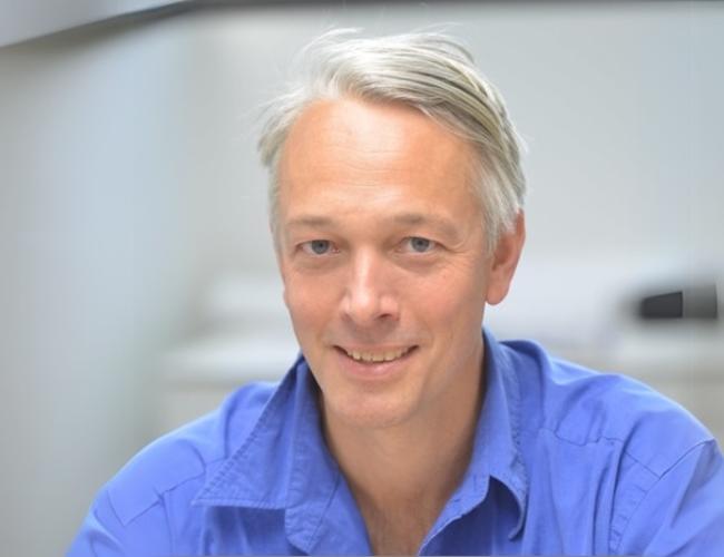 A headshot of Alexander Hoffman, Ph.D., who is pictured smiling and wearing a blue dress shirt.
