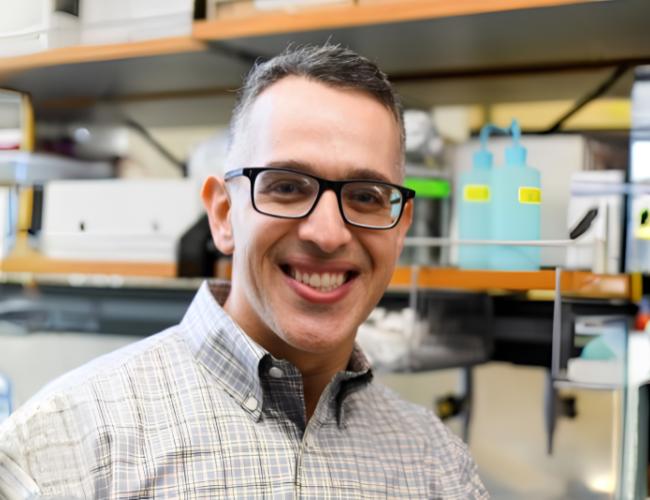 Headshot of Dr. Albert Almada in glasses and a plaid button up shirt in his lab