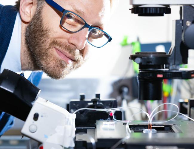 UCLA Scientist Dino Di Carlo leans over equipment in a lab and smiles at camera. 