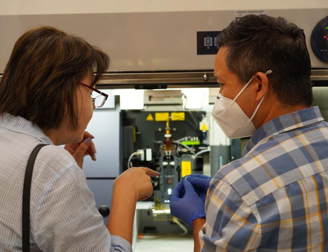 Two individuals photographed from behind, conversing in a UCLA lab. 