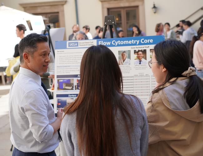 Event participants gather around a poster board in a UCLA courtyard.
