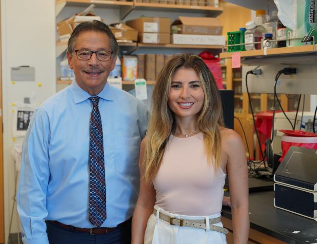 Scientist Donald Kohn on the left wearing a blue button down shirt and scientist Eva Segura on the right wearing a peach shirt; both are in the lab