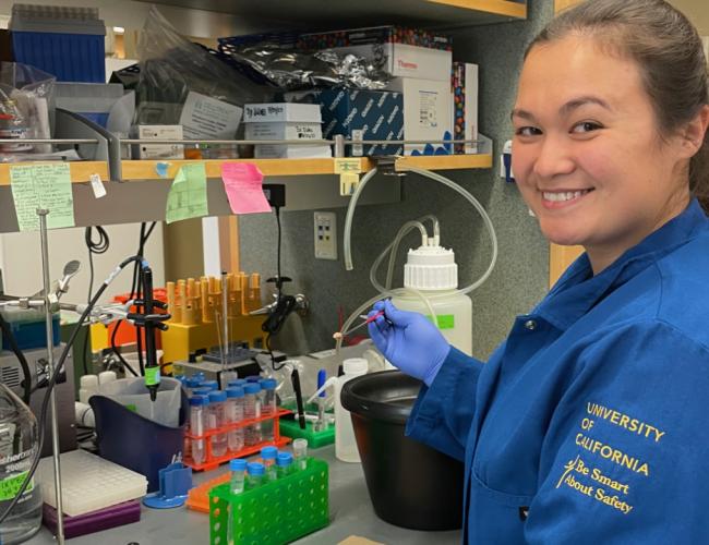 Woman in blue lab coat smiling while working with laboratory equipment and test tubes