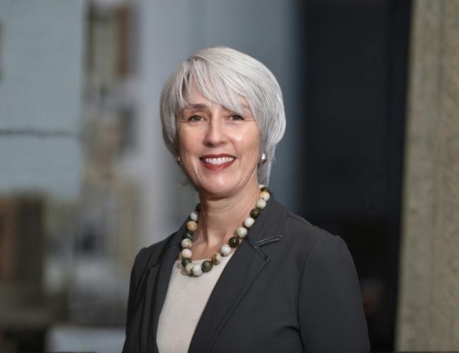 Headshot of Margaret Goodell in a dark blazer, light top and necklace against a faded background