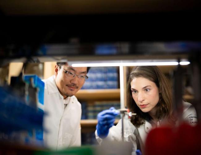 A photo that shows Dr. John Lee and Galina Semenova in a laboratory, working together on setting up lab equipment. Both scientists are dressed in white lab coats. 