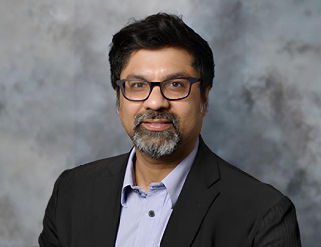 Headshot of Sanjeev Kumar wearing glasses, a dark blazer and light blue button up